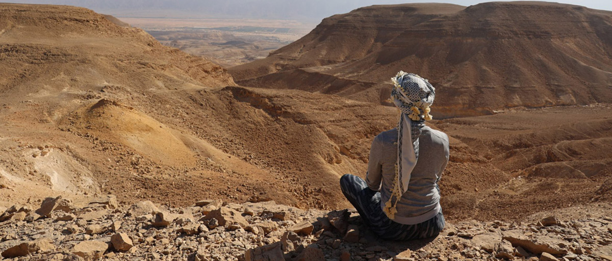 Auf diesem Bild sieht man eine Frau mit Turban in der Wüste, die in die Ferne schaut.
