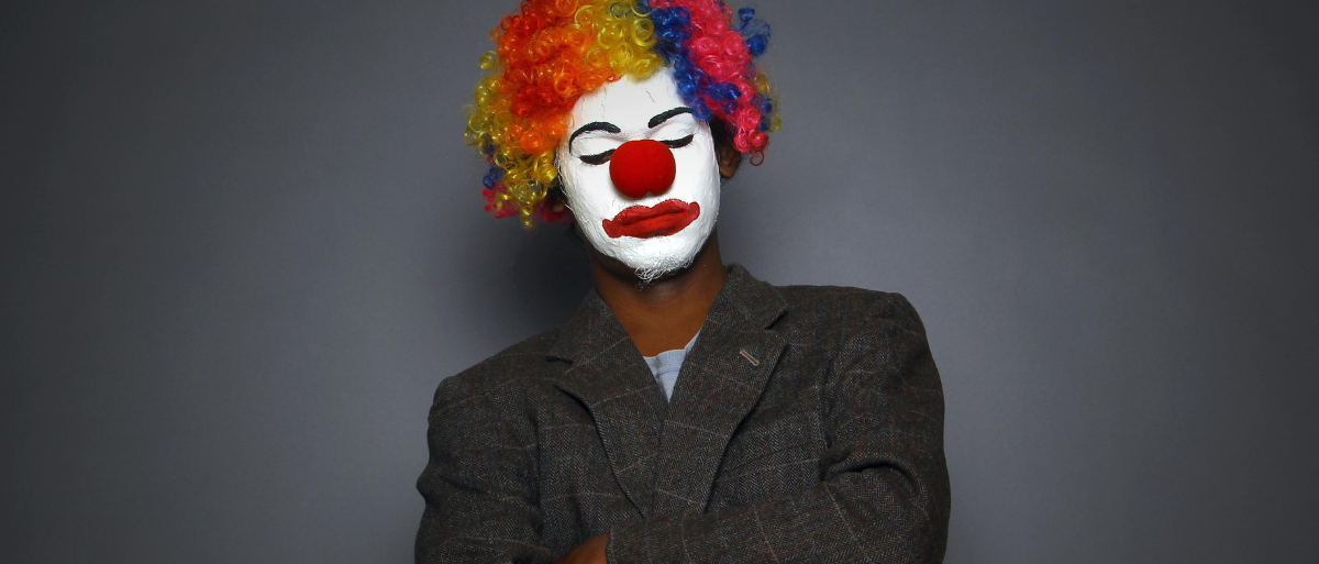 100 Jahre Caritaswissenschaft (3) Auf dem Bild ist ein Clown mit verschränkten Armen und lässiger Haltung zu sehen, der die Augen geschlossen hat und eine bunte Perücke trägt.