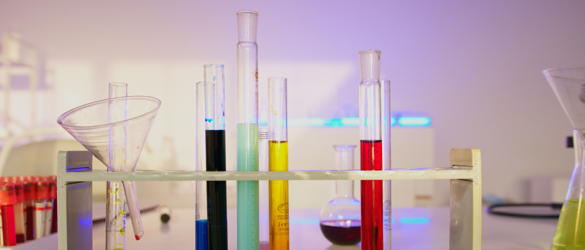 Experimentaltheologie Man sieht verschiedene Glasampullen mit bunten Flüssigkeiten, die in einem Holzständer stehen.
